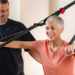Ältere Frauen trainieren im Fitnessstudio mit Hilfe des Trainers ihre Arme mit TRX-Fitnessbändern