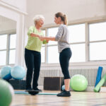 Trainer hilft älterer Frau auf Bosu-Balance-Trainingsplattform